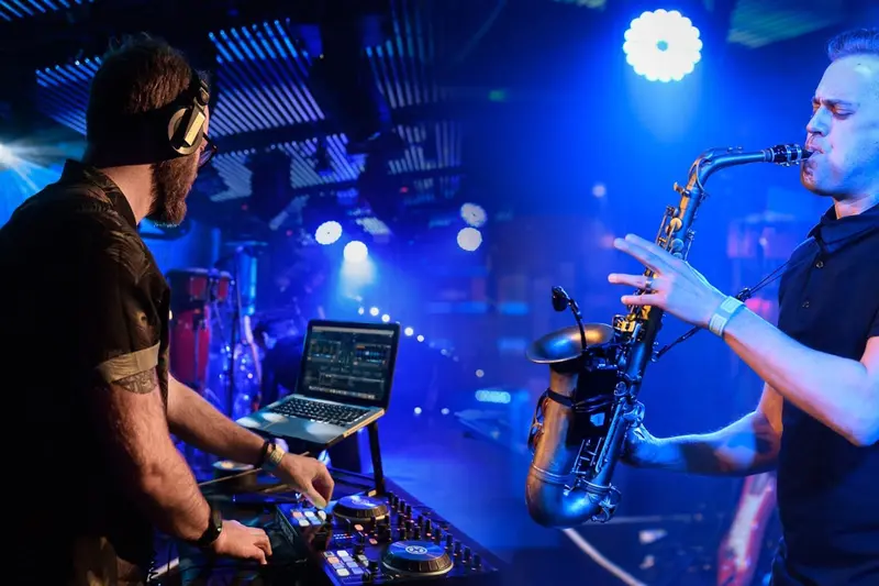 DJ and saxophonist performing together under blue lights at an evening party