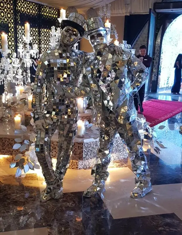 Two walkabout performers in mirror suits greeting guests at the entrance of a candlelit event venue